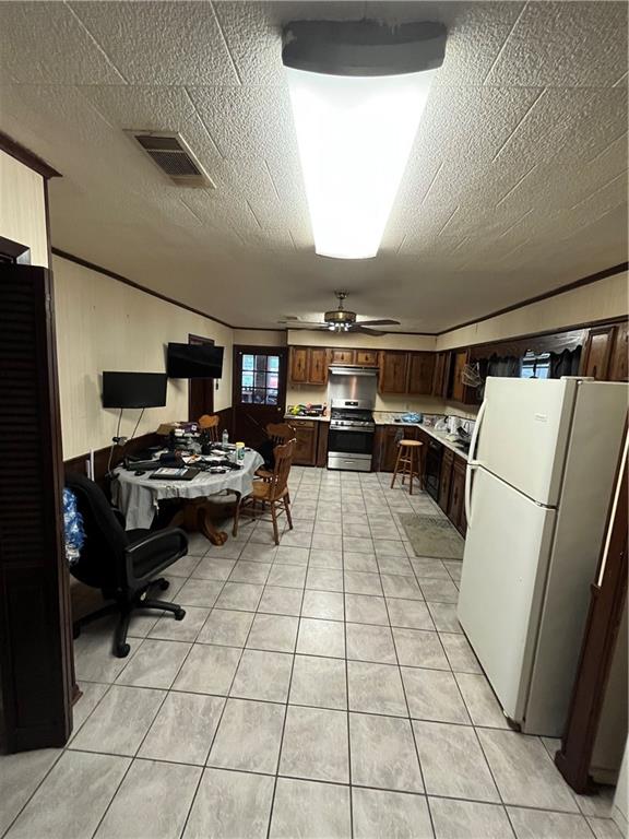 kitchen with ceiling fan, stainless steel stove, white refrigerator, a textured ceiling, and light tile patterned floors