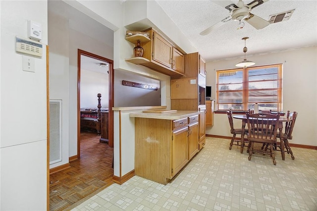 kitchen featuring ceiling fan, light parquet flooring, hanging light fixtures, and a textured ceiling