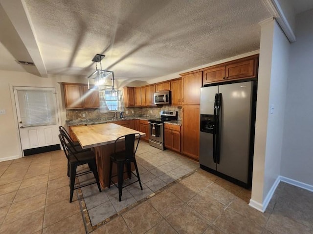 kitchen featuring a kitchen bar, butcher block counters, pendant lighting, stainless steel appliances, and tasteful backsplash