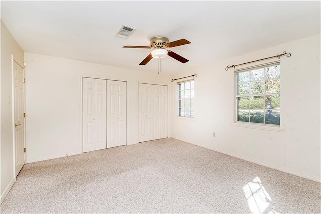 unfurnished bedroom with light carpet, two closets, and ceiling fan