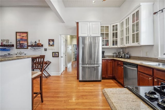 kitchen with sink, a breakfast bar, appliances with stainless steel finishes, white cabinetry, and light wood-type flooring