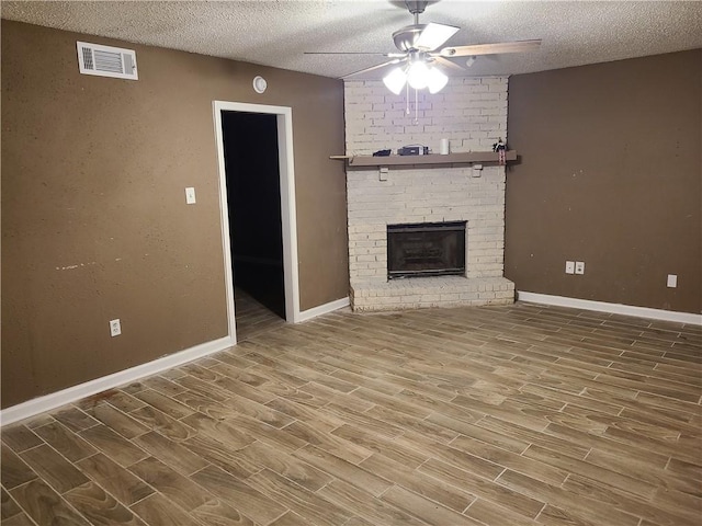 unfurnished living room with hardwood / wood-style floors, ceiling fan, a brick fireplace, and a textured ceiling