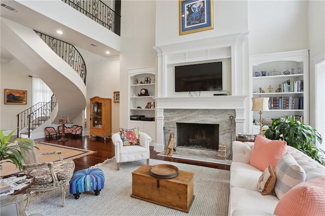 living room with hardwood / wood-style floors, a towering ceiling, built in features, and a high end fireplace