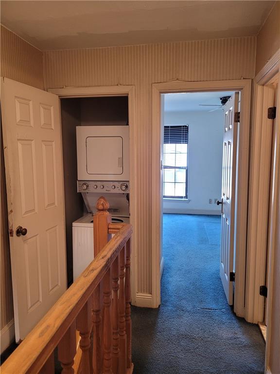 corridor with stacked washer and clothes dryer and dark carpet