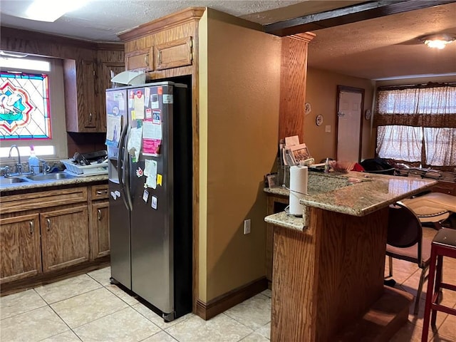 kitchen featuring light tile flooring, stainless steel fridge, a breakfast bar area, stone counters, and sink