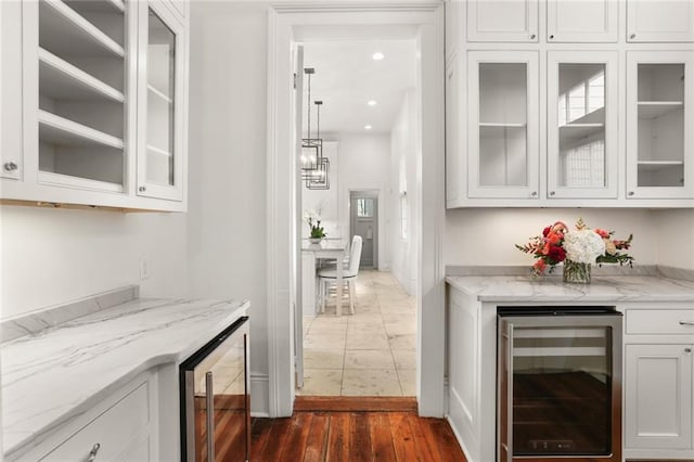 bar with light stone counters, dark hardwood / wood-style flooring, white cabinets, and beverage cooler