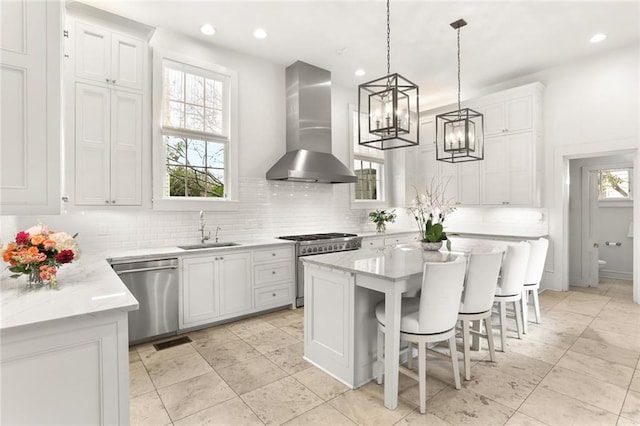 kitchen featuring pendant lighting, stainless steel appliances, sink, white cabinetry, and wall chimney exhaust hood