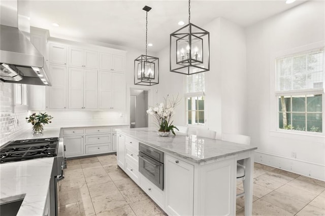 kitchen featuring decorative light fixtures, white cabinets, stainless steel appliances, backsplash, and wall chimney range hood