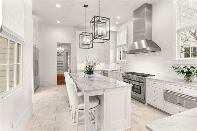 kitchen with wall chimney exhaust hood, white cabinets, appliances with stainless steel finishes, and a wealth of natural light