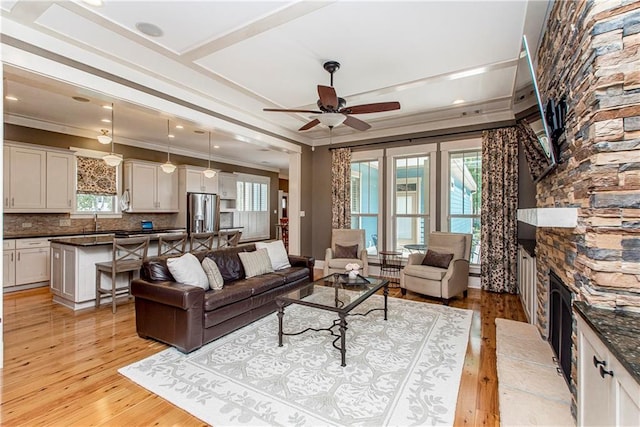 living room featuring a stone fireplace, ceiling fan, a healthy amount of sunlight, and light hardwood / wood-style flooring