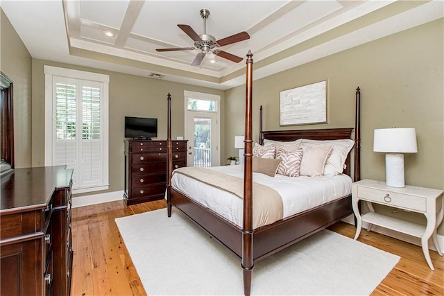 bedroom with a raised ceiling, coffered ceiling, ceiling fan, and light wood-type flooring