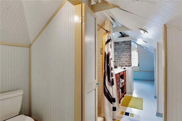 bathroom featuring lofted ceiling with beams, toilet, vanity, and brick wall