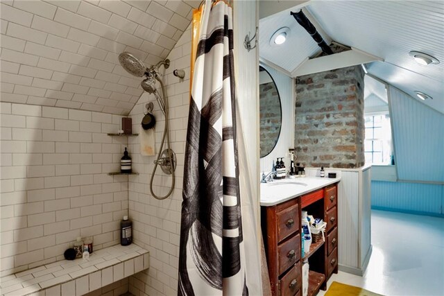 bathroom with large vanity, a tile shower, and vaulted ceiling