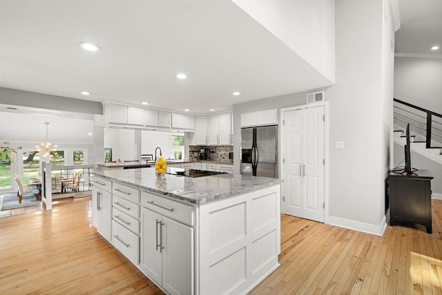 kitchen featuring light hardwood / wood-style flooring, white cabinetry, stainless steel fridge with ice dispenser, and light stone counters