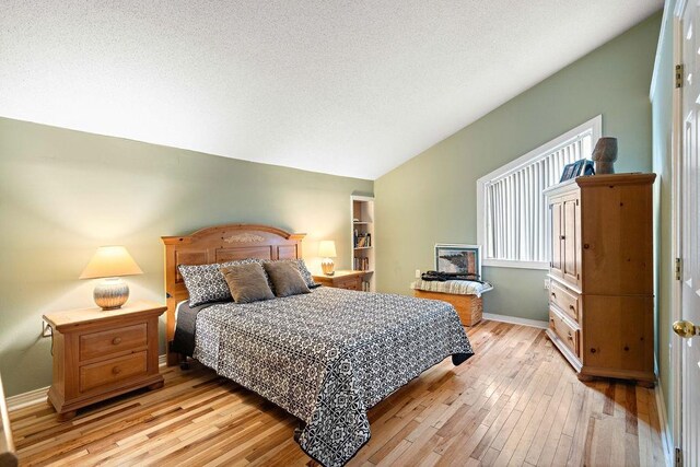 bedroom featuring a textured ceiling, lofted ceiling, and light wood-type flooring