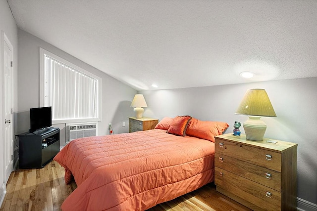 bedroom featuring an AC wall unit, light hardwood / wood-style floors, vaulted ceiling, and a textured ceiling