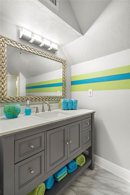 bathroom featuring vanity, a textured ceiling, lofted ceiling, and tile patterned flooring