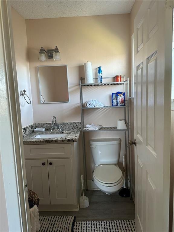 bathroom featuring vanity, a textured ceiling, hardwood / wood-style flooring, and toilet