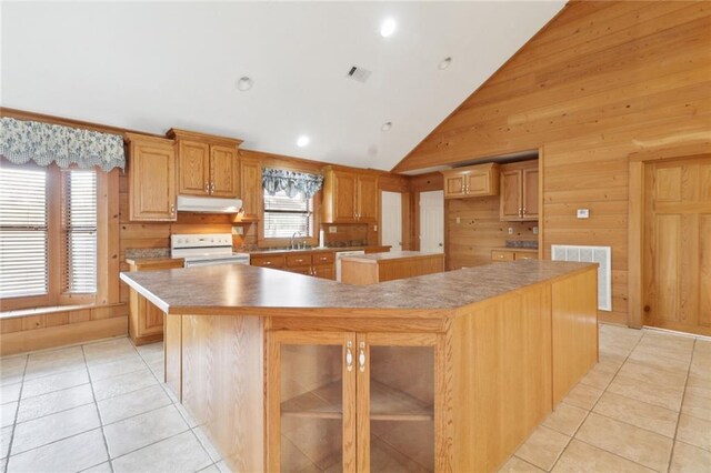 kitchen with light tile patterned flooring, a center island, wood walls, and white appliances