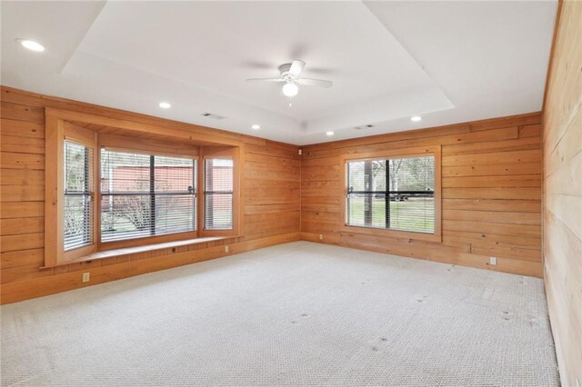 carpeted empty room featuring a raised ceiling, wooden walls, and ceiling fan