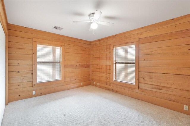 carpeted spare room featuring wood walls and ceiling fan