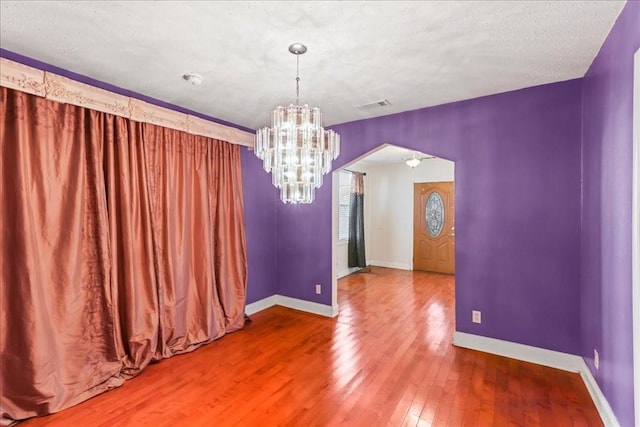 spare room with an inviting chandelier, hardwood / wood-style floors, and a textured ceiling