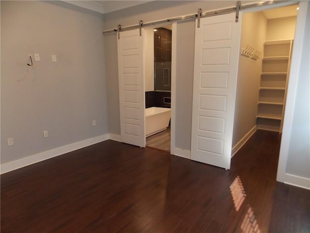 unfurnished bedroom with a barn door, a spacious closet, dark hardwood / wood-style floors, and ornamental molding