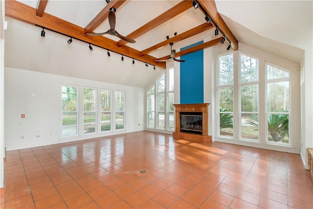 unfurnished living room with ceiling fan, a healthy amount of sunlight, beamed ceiling, high vaulted ceiling, and light tile floors