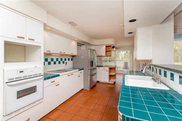 kitchen featuring white oven, light tile flooring, white cabinetry, backsplash, and sink