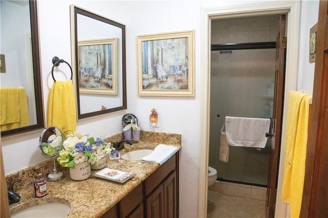 bathroom featuring double sink vanity, tile floors, toilet, and a shower with door