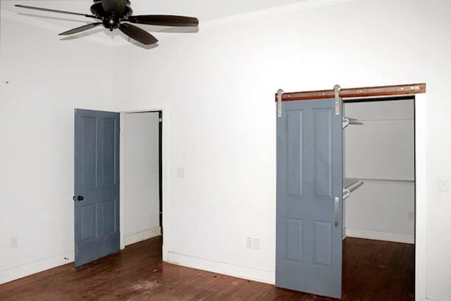 unfurnished bedroom featuring a barn door, ceiling fan, crown molding, and dark hardwood / wood-style floors