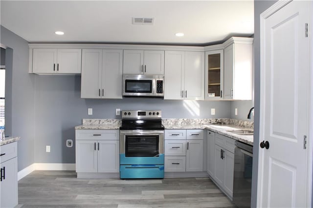 kitchen with light stone countertops, light wood-type flooring, stainless steel appliances, and sink