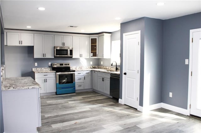 kitchen featuring gray cabinetry, sink, light hardwood / wood-style flooring, light stone countertops, and stainless steel appliances