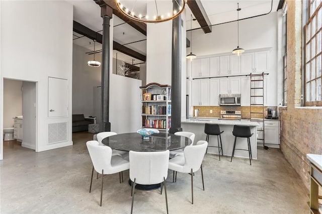 dining area with a notable chandelier, beamed ceiling, and a towering ceiling