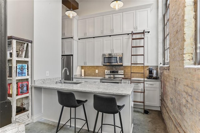 kitchen with a kitchen bar, light stone countertops, appliances with stainless steel finishes, white cabinets, and sink