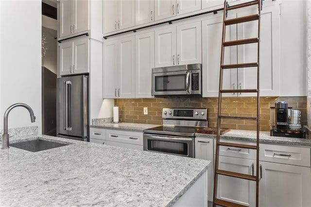 kitchen featuring light stone countertops, white cabinetry, backsplash, appliances with stainless steel finishes, and sink