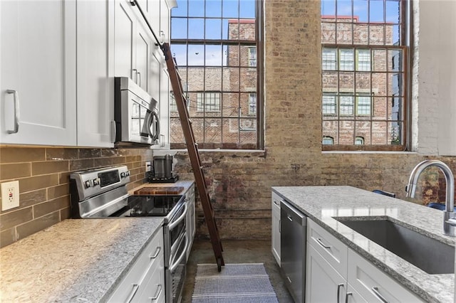 kitchen with sink, stainless steel appliances, light stone counters, and white cabinetry