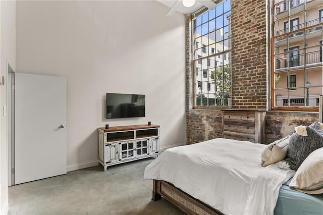 bedroom with a towering ceiling, ceiling fan, and brick wall