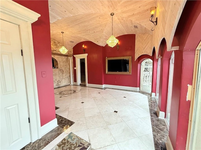 foyer entrance featuring arched walkways, a notable chandelier, visible vents, vaulted ceiling, and baseboards