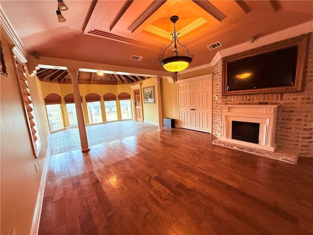 unfurnished living room featuring a fireplace with raised hearth, wood finished floors, visible vents, a raised ceiling, and crown molding