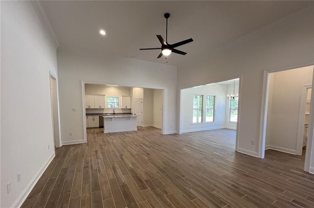 unfurnished living room with ornamental molding, sink, ceiling fan with notable chandelier, and dark wood-type flooring