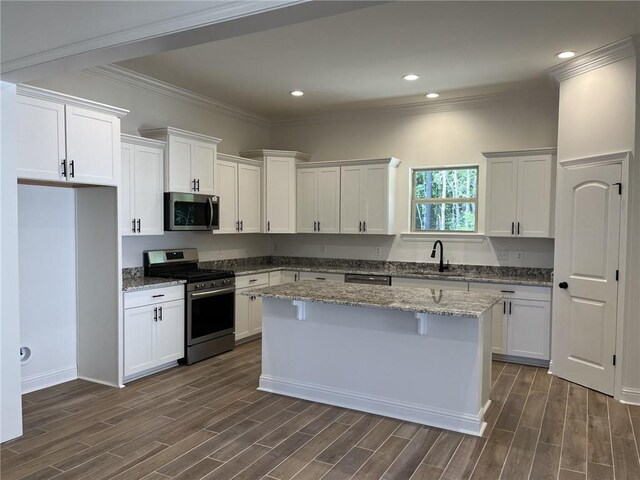 kitchen with light stone counters, white cabinets, a kitchen island, dark wood-type flooring, and appliances with stainless steel finishes