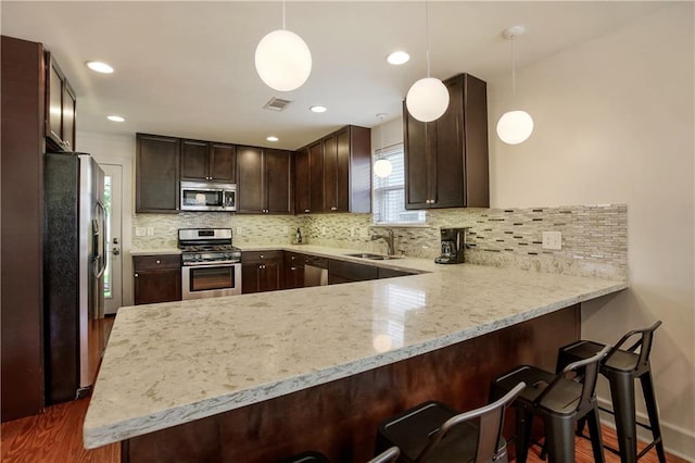 kitchen featuring appliances with stainless steel finishes, dark hardwood / wood-style floors, light stone countertops, and kitchen peninsula