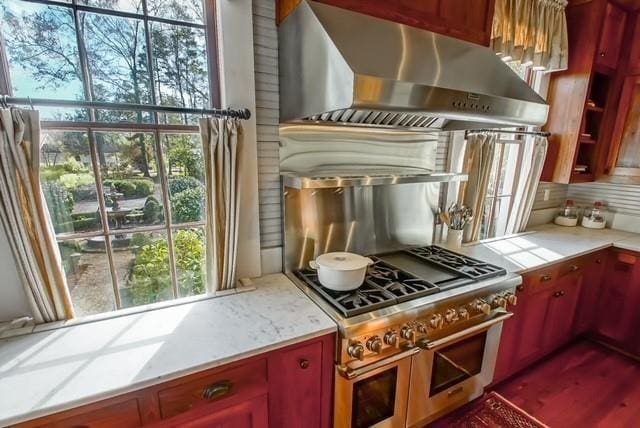 kitchen featuring backsplash, double oven range, wall chimney range hood, and a wealth of natural light