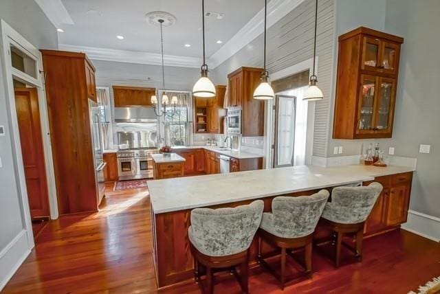 kitchen featuring kitchen peninsula, hanging light fixtures, stainless steel appliances, dark hardwood / wood-style floors, and wall chimney range hood