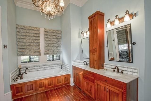 bathroom with double sink vanity, a washtub, a chandelier, ornamental molding, and wood-type flooring