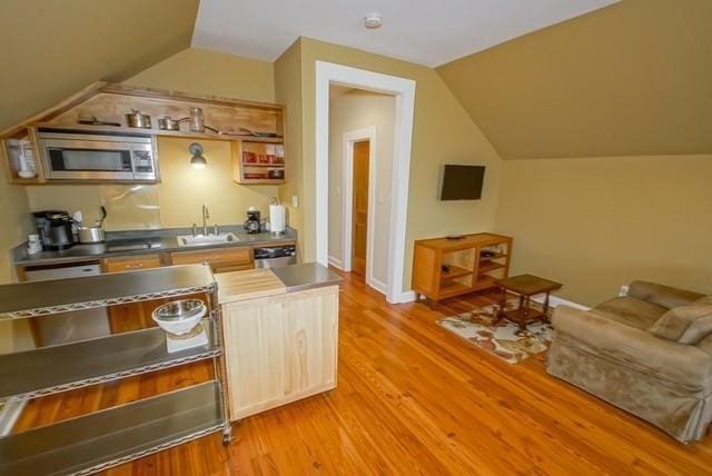 kitchen with light hardwood / wood-style flooring, stainless steel counters, vaulted ceiling, stainless steel microwave, and sink