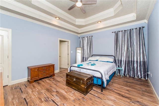 bedroom featuring a tray ceiling, ornamental molding, hardwood / wood-style floors, and ceiling fan