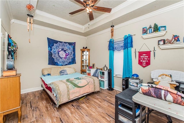 bedroom with hardwood / wood-style flooring, ceiling fan, a textured ceiling, ornamental molding, and a raised ceiling