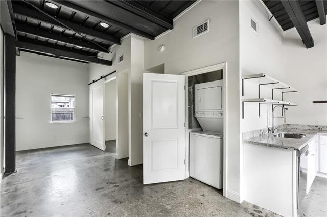 interior space with a barn door, light stone countertops, stacked washer / dryer, white cabinets, and sink